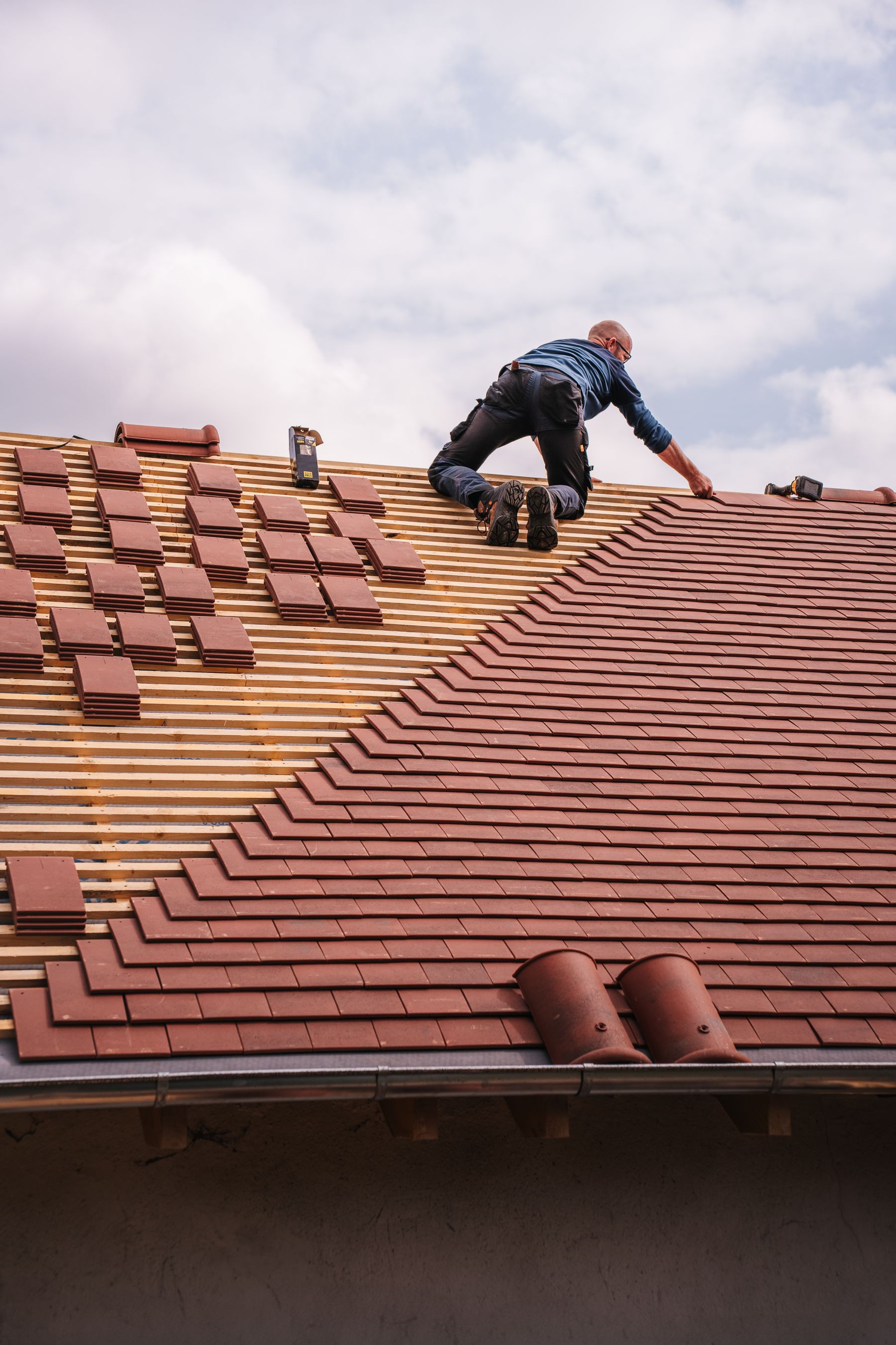 A roofer installing tiles on a residential roof.